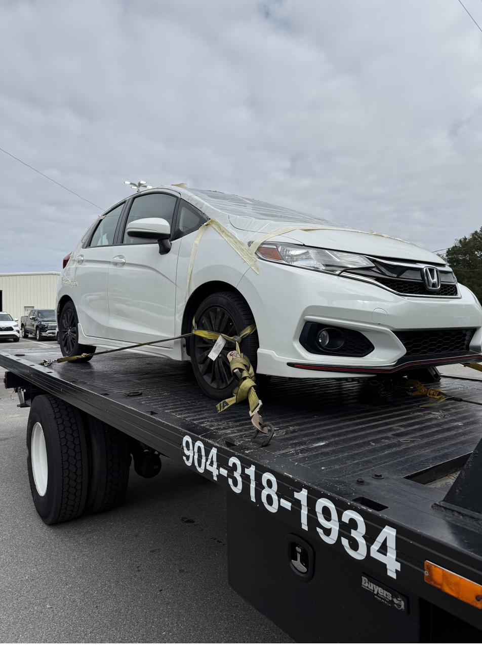 White Honda Fit wrapped for transport on a flatbed
