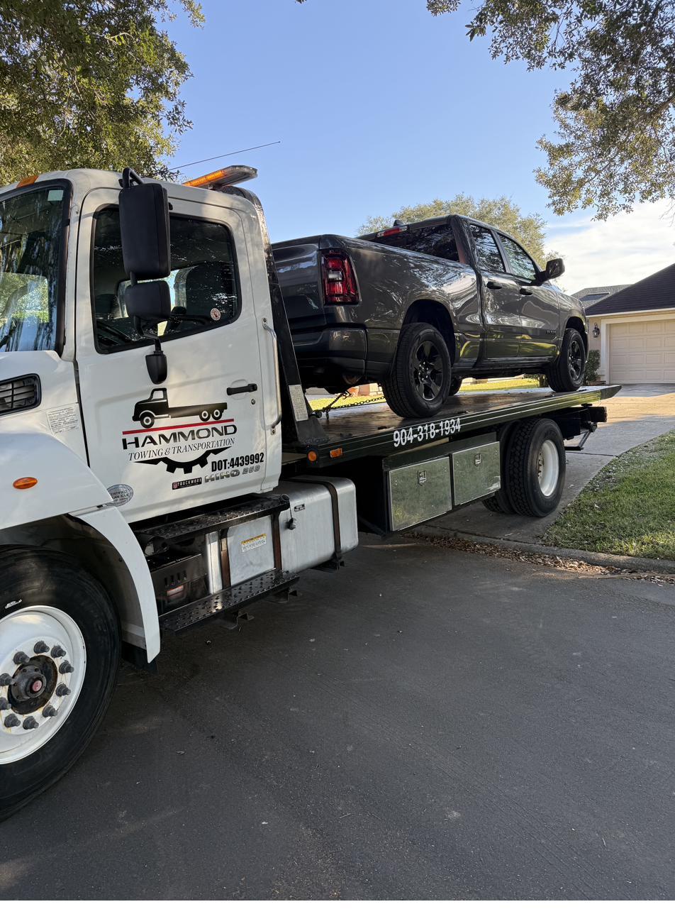 Hammond Towing rollback truck with a Ram 1500 pickup loaded in a driveway